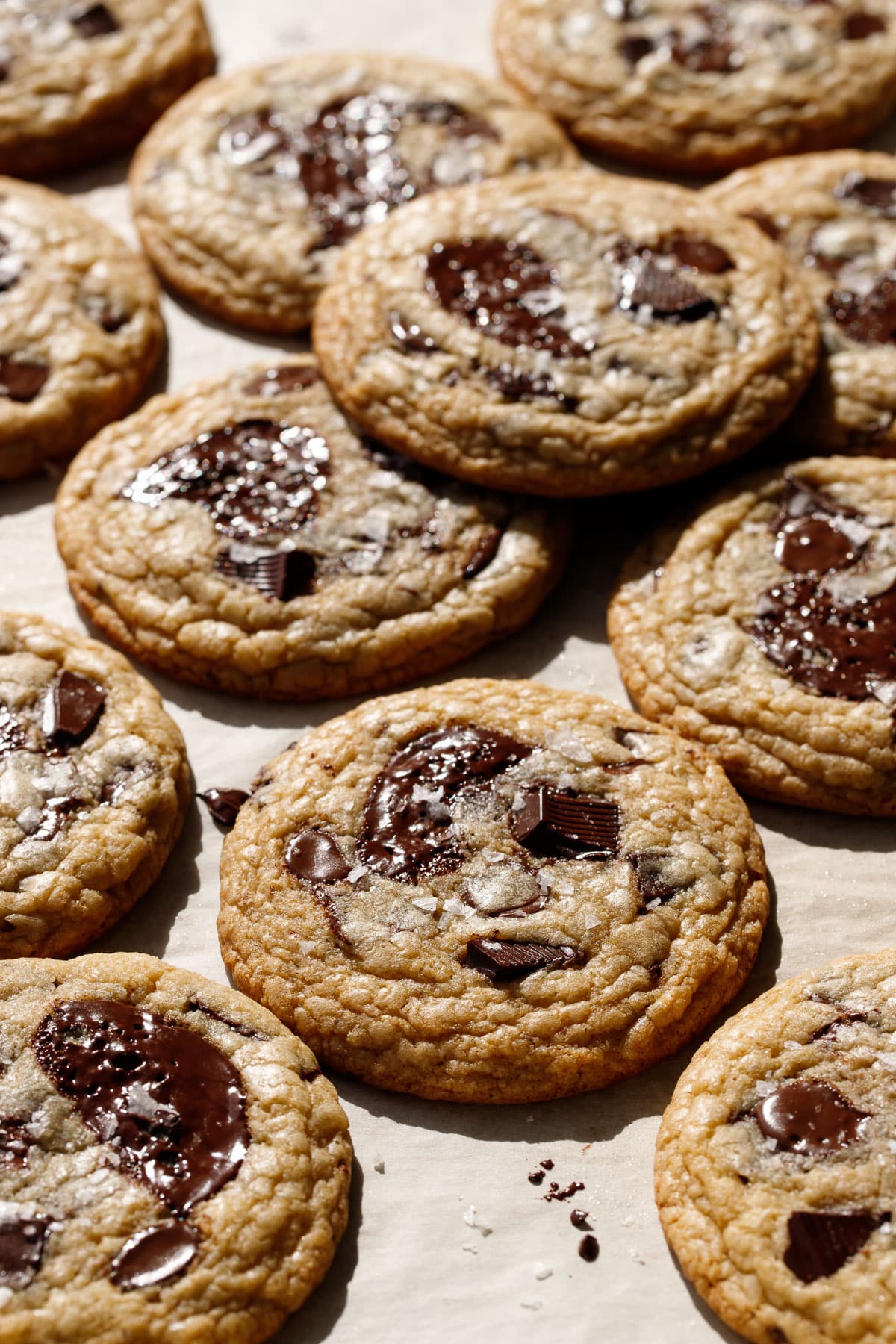 Messy arrangement of Amaretto Chocolate Chip Cookies, with shiny melty puddles of chocolate and visible flakes of sea salt.