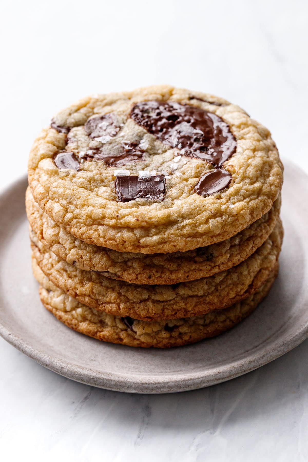 Stack of 4 Amaretto Chocolate Chip Cookies on a ceramic plate, light reflecting off the melted chocolate puddles on top.