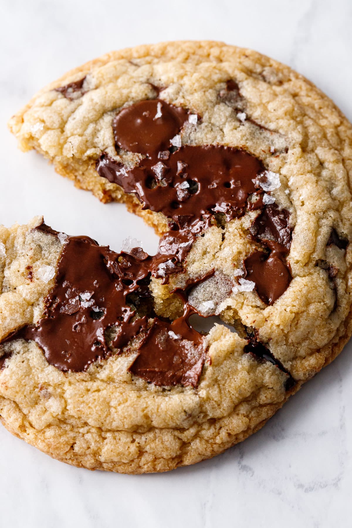 Extreme closeup of one Amaretto Chocolate Chip Cookies broken in half, a thread of melted chocolate stretching between halves.