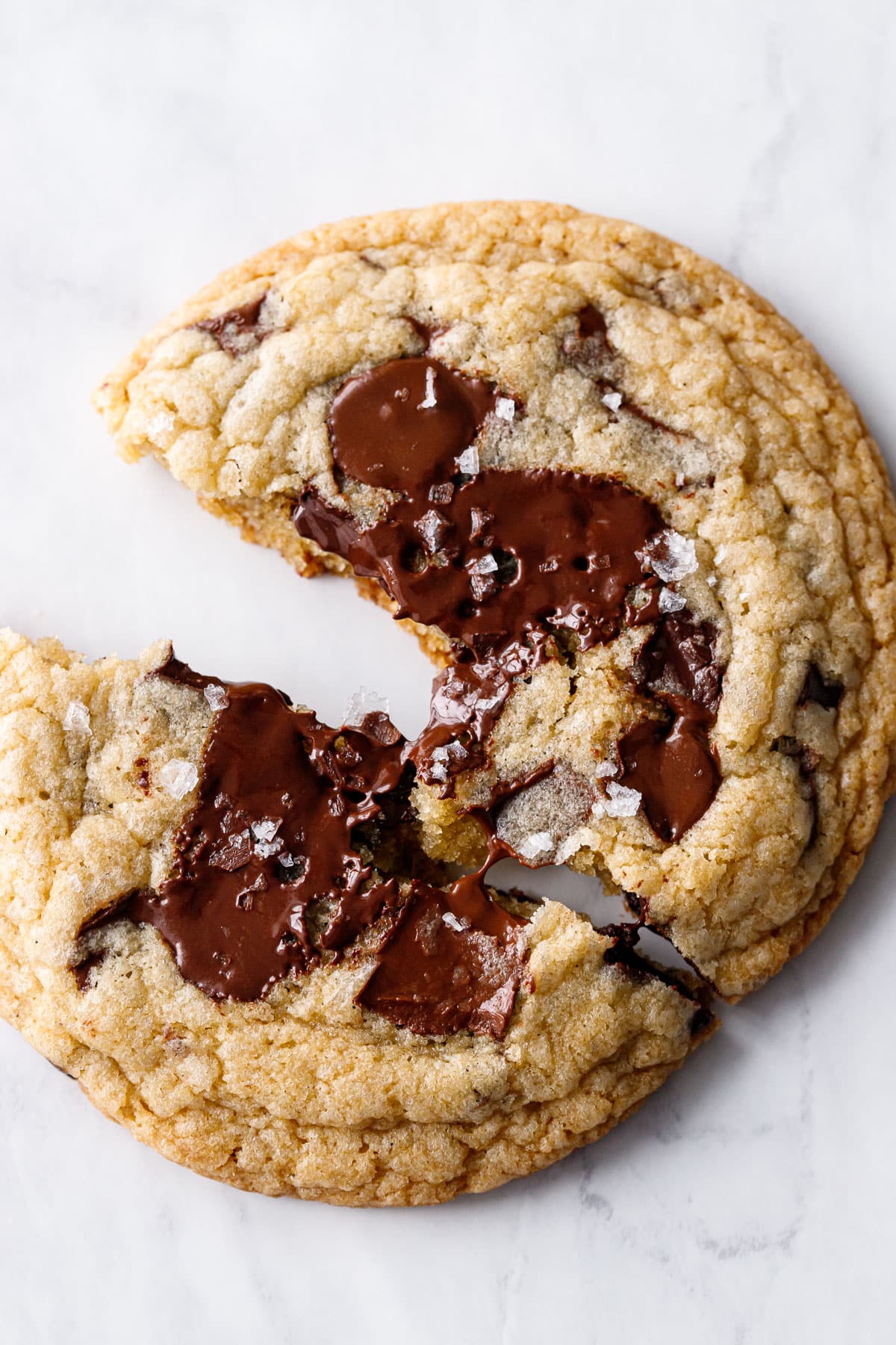 Extreme closeup of one Amaretto Chocolate Chip Cookies broken in half, a thread of melted chocolate stretching between halves.