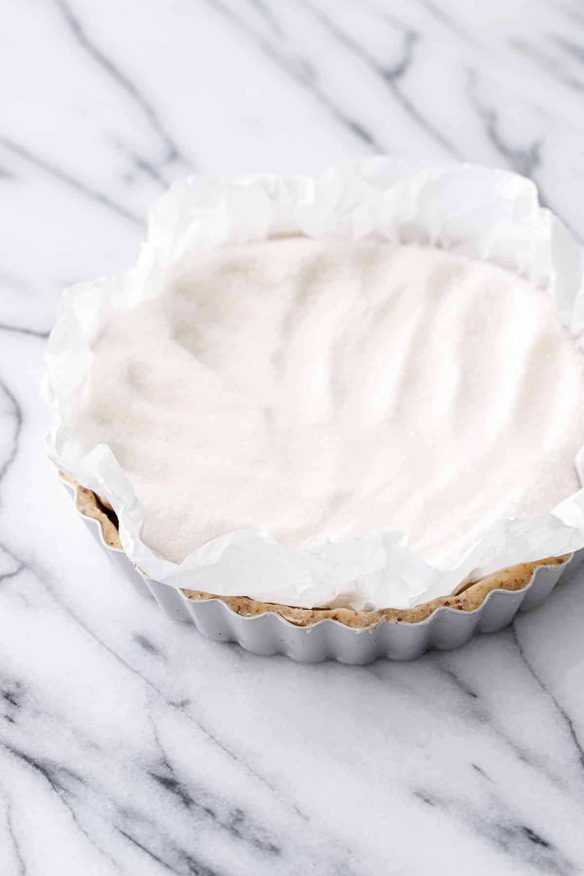 Filling the unbaked, parchment lined tart shell with sugar instead of pie weights.