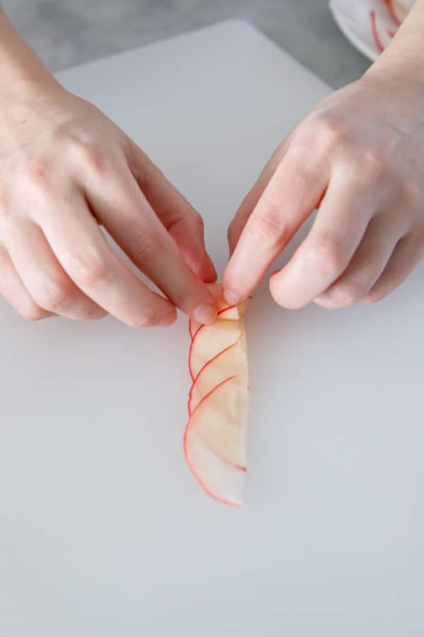 Rolling up a row of paper-thin apple slices to form an apple rose garnish.