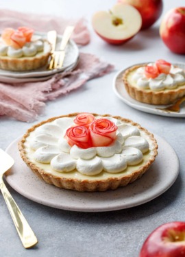 Caramel Apple Mousse Tart on a ceramic plate, with smaller tartlets and red apples in the background.