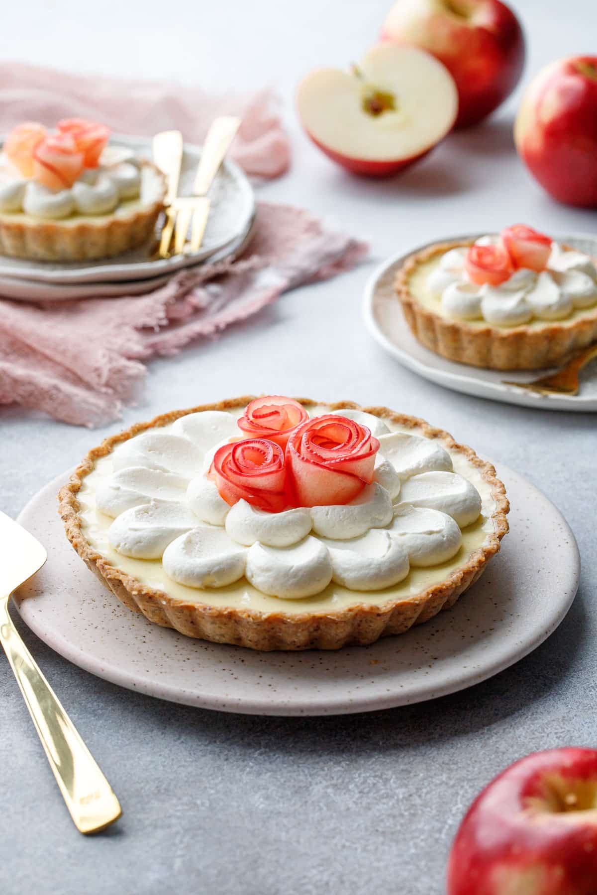 Caramel Apple Mousse Tart on a ceramic plate, with smaller tartlets and red apples in the background.