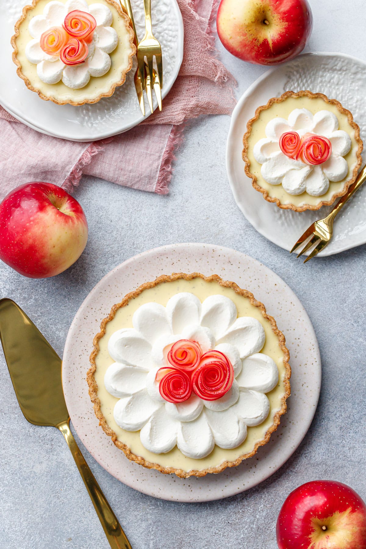 Overhead, one larger Caramel Apple Mousse Tart and two smaller tartlets with apple rose decorations, red apples scattered around.