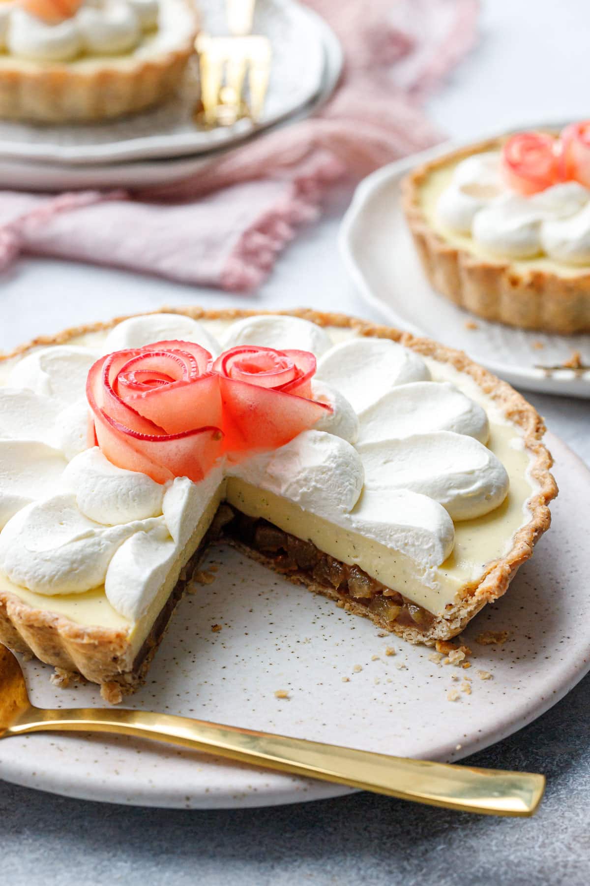 Caramel Apple Mousse Tart with a slice taken out to show the distinct layers, with a gold pie server and two more smaller tarts in the background.