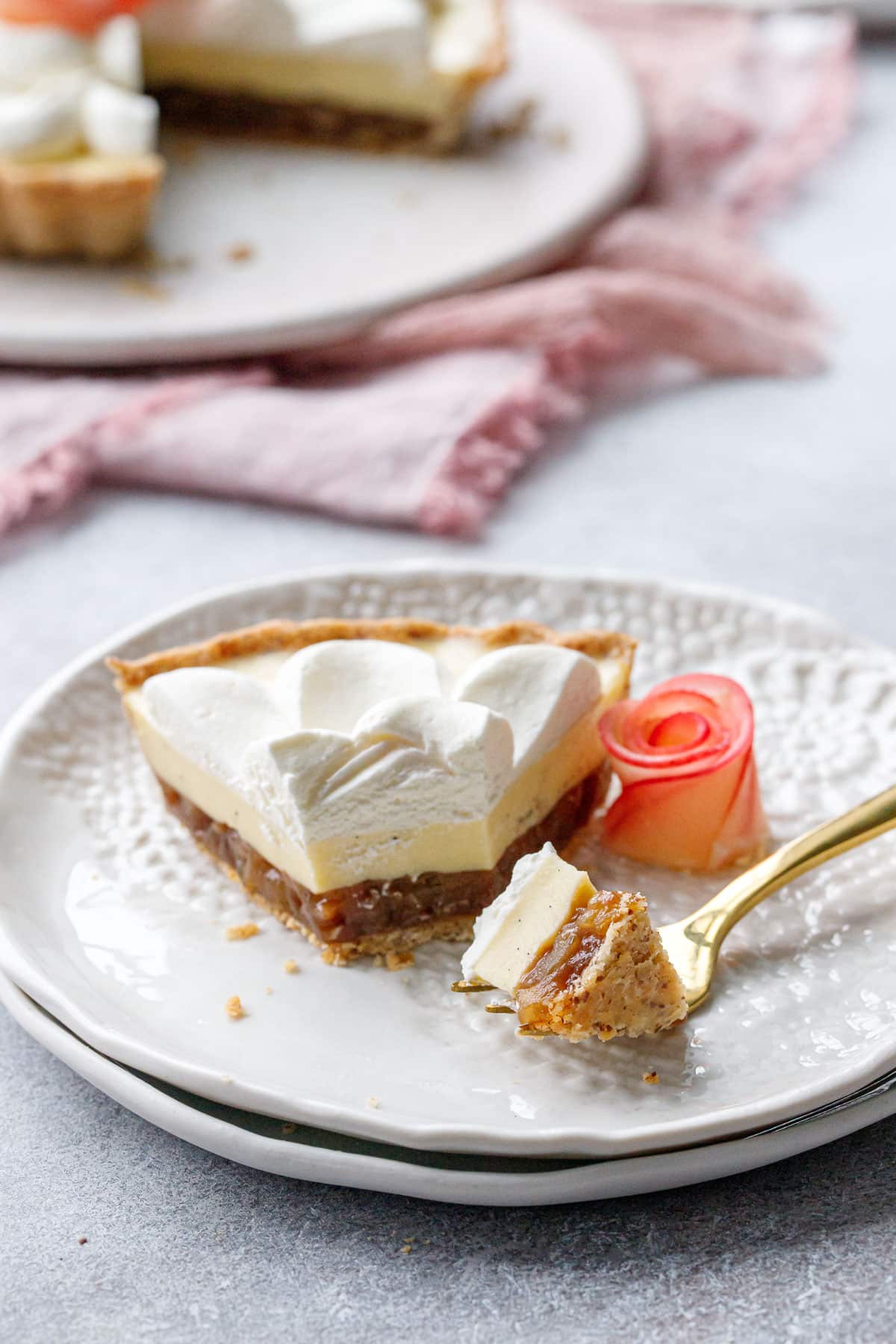 Slice of Caramel Apple Mousse Tart on a white lace plate with a gold fork and a bite taken out.