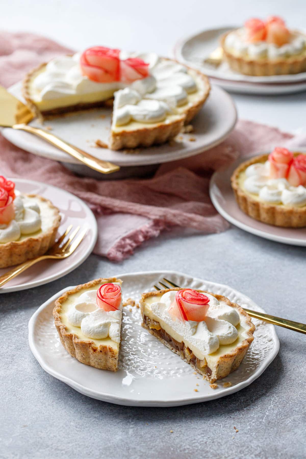 Messy scene featuring Caramel Apple Mousse Tarts, one big tart with a slice taken out and multiple smaller tartlets, one cut in half to show layers.