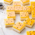 Square-cut Passionfruit Cheesecake Bars with a bright yellow top layer and black passionfruit seeds on a marble background.
