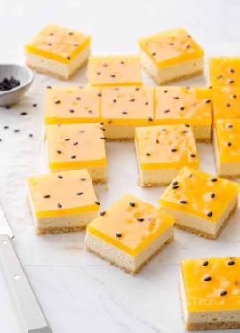 Square-cut Passionfruit Cheesecake Bars with a bright yellow top layer and black passionfruit seeds on a marble background.