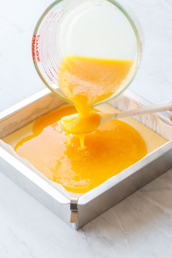 Pouring the passionfruit gelatin over a spoon or spatula on top of the baked cheesecake layer.