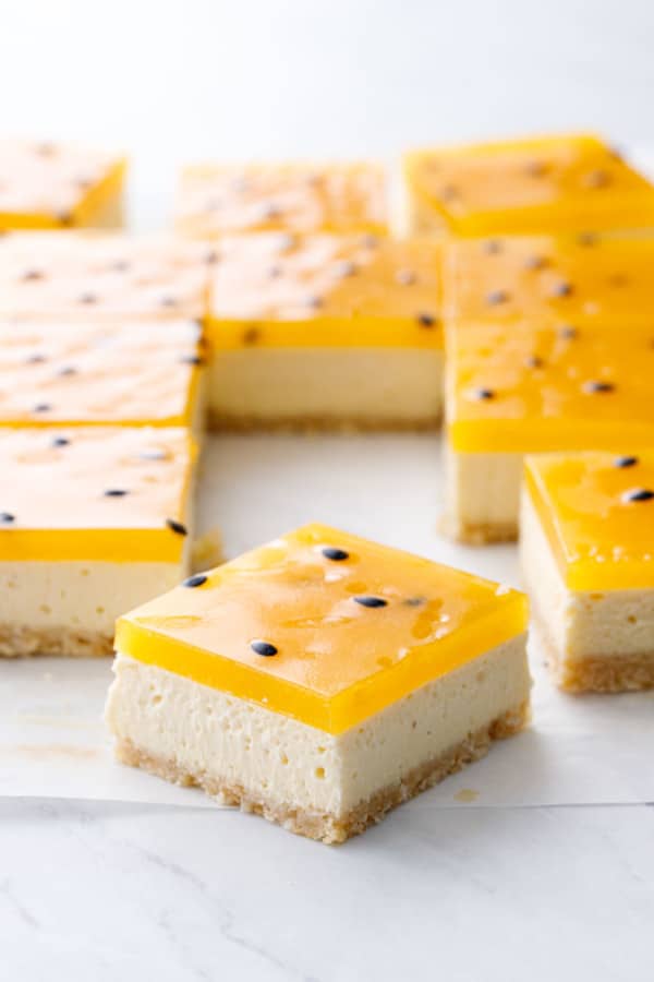 Closeup, cut Passionfruit Cheesecake Bar showcasing the perfect layers of crust, cheesecake, and passionfruit gelatin with black seeds.