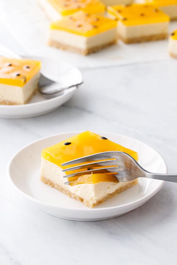 Plate with square of Passionfruit Cheesecake, fork slicing down through to show the various textures.