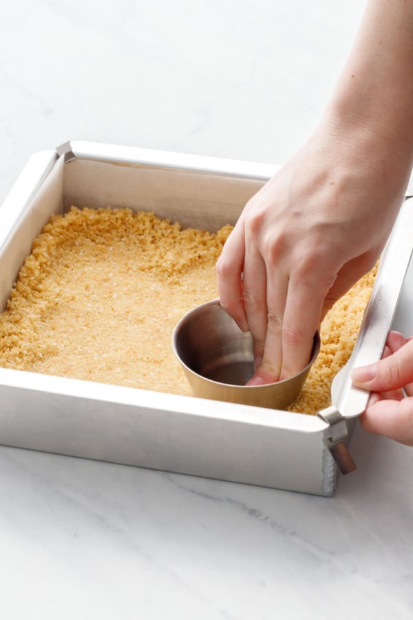 Using a flat-bottomed measuring cup to press the cookie crust into the baking pan.