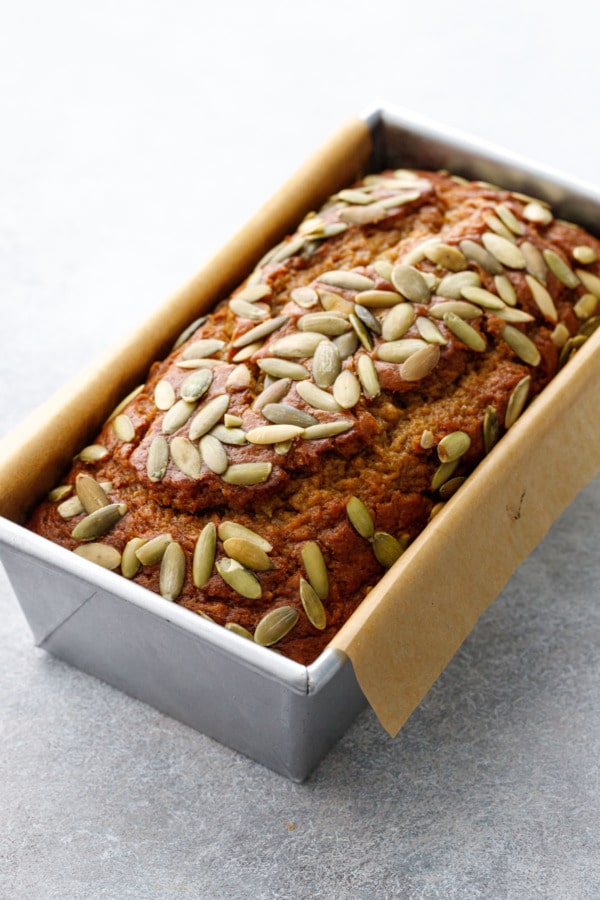 Metal loaf pan with Spiced Pumpkin Banana Bread, pumpkin seeds baked on top.