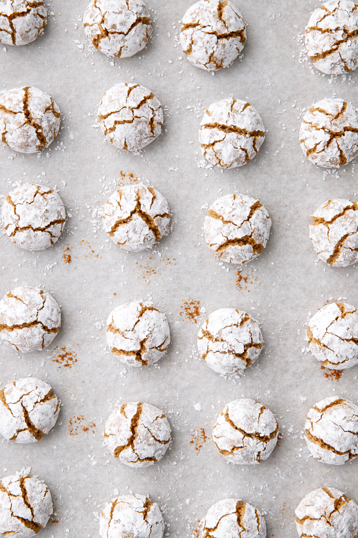 Overhead, neat rows of baked Gingerbread Amaretti Cookies coated in powdered sugar with a crackled appearance.