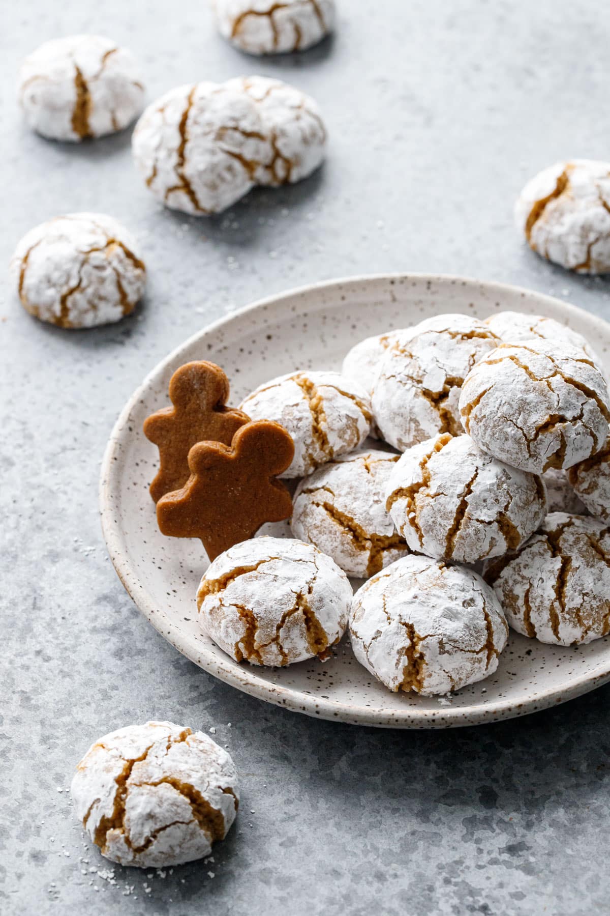 Small plate with a stack of Gingerbread Amaretti Cookies and two gingerbread men on the side.