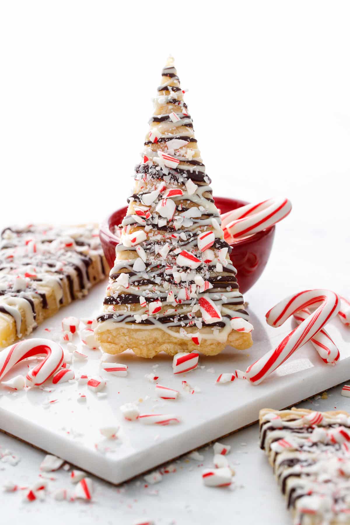Christmas-tree shaped Peppermint Bark Shortbread cookies, cut into triangles and drizzled with white and dark chocolate and crushed candy cane pieces.
