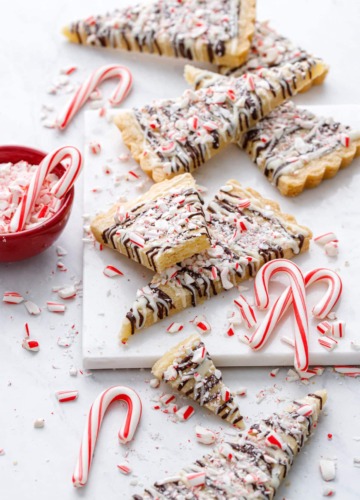 Peppermint Bark Shortbread on marble, with messy bits of candy canes and a red bowl of crushed candy canes on the side.