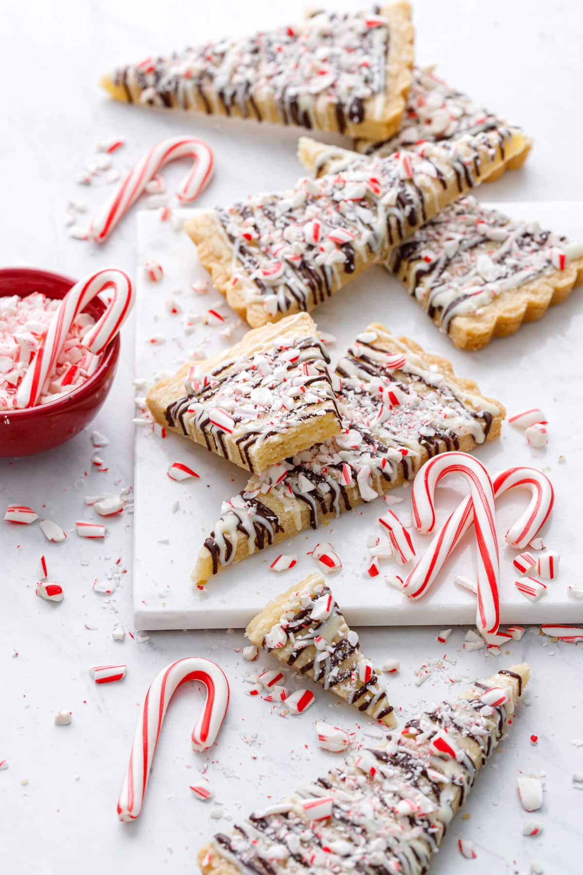 Peppermint Bark Shortbread on marble, with messy bits of candy canes and a red bowl of crushed candy canes on the side.