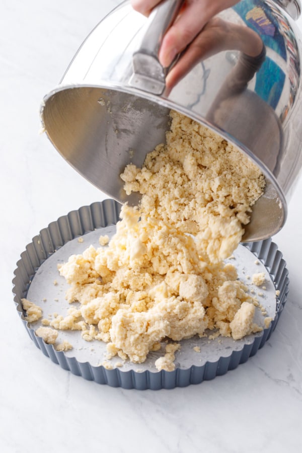 Dumping the crumbly shortbread dough into a parchment-lined tart pan.