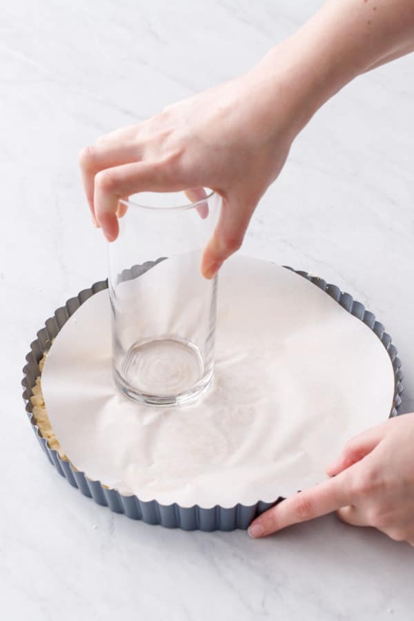 Using a glass and a piece of parchment to press the shortbread dough smoothly into an even layer.