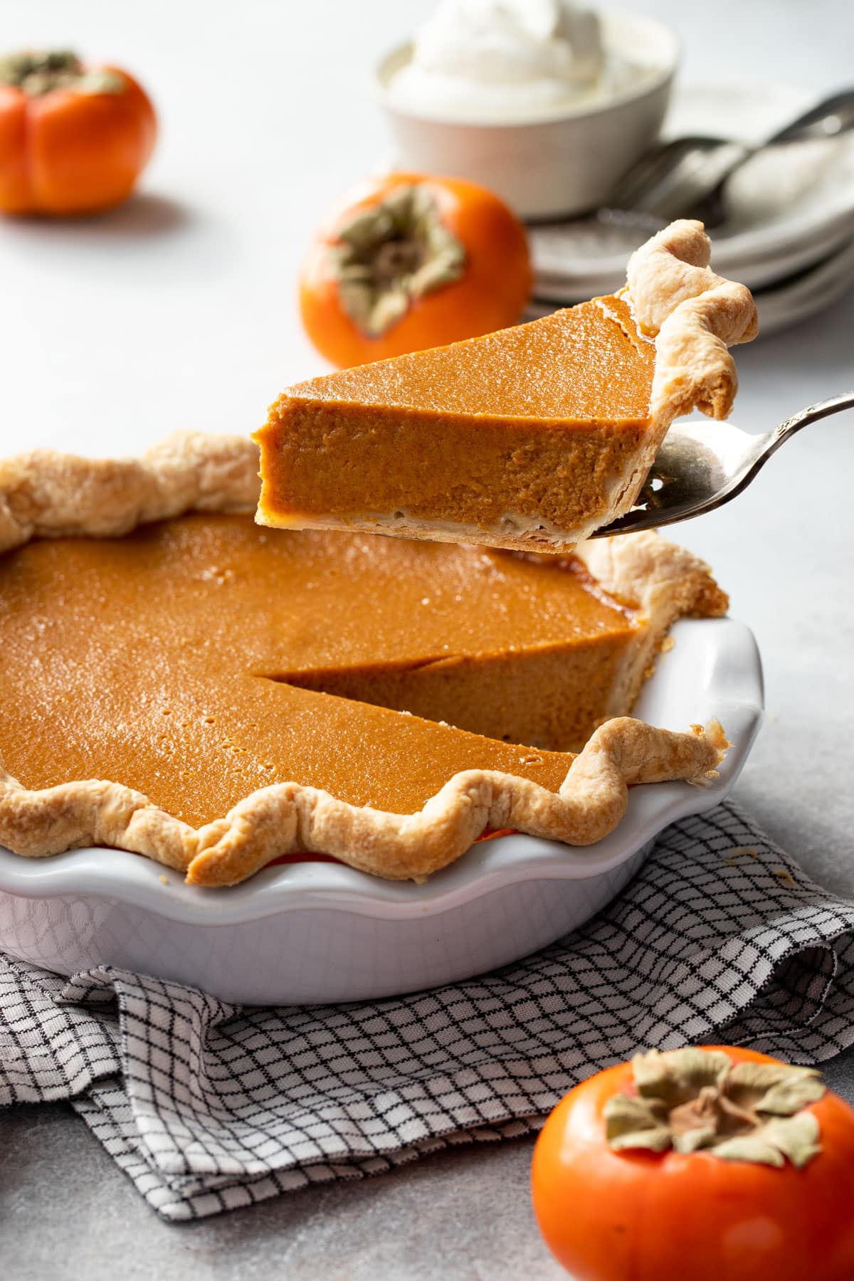 Persimmon Pie in a white ruffled pie pan with a slice being lifted out by a pie server.