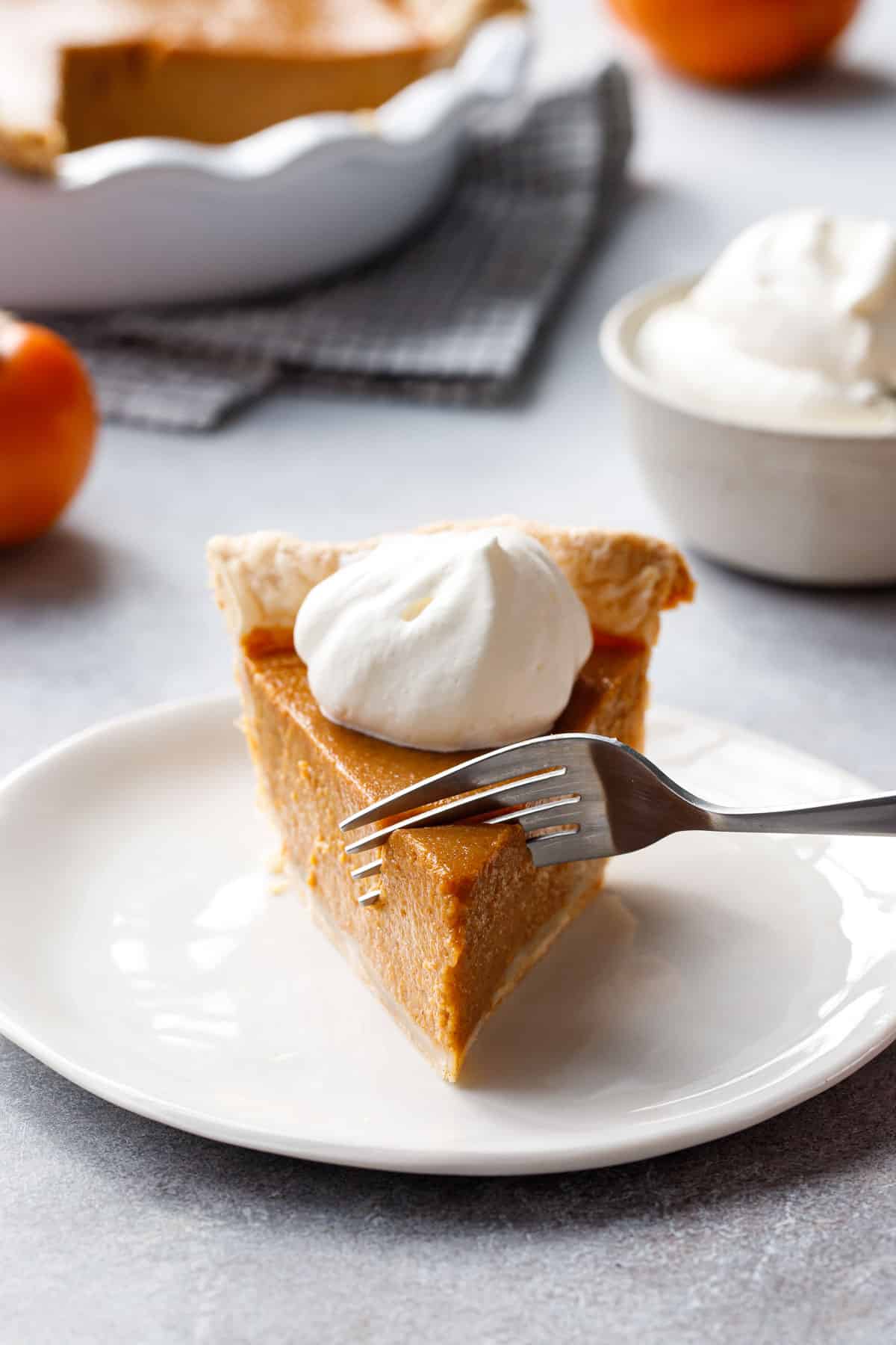 Fork cutting a bite out of a slice of Persimmon Pie on a white ceramic plate.