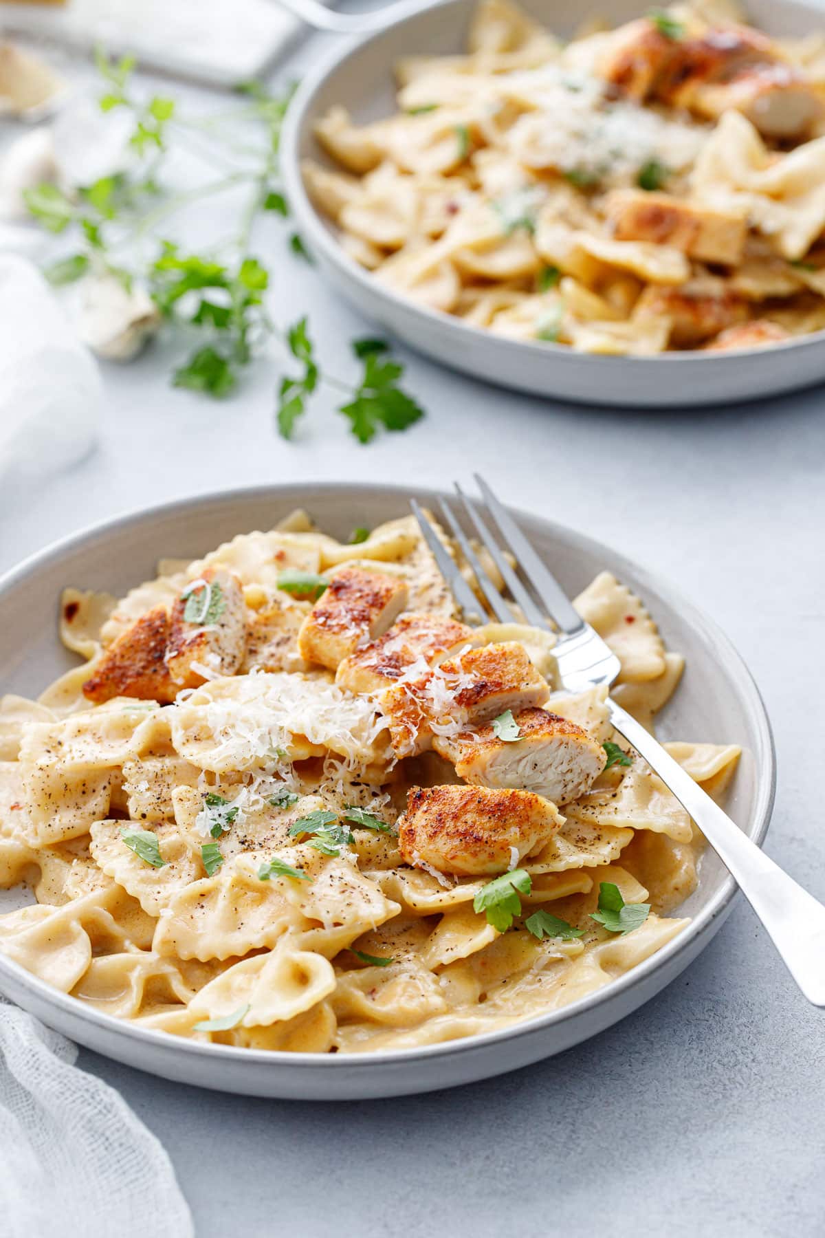 Two gray shallow bowls with Creamy Garlic Pasta topped with browned chicken tenders.