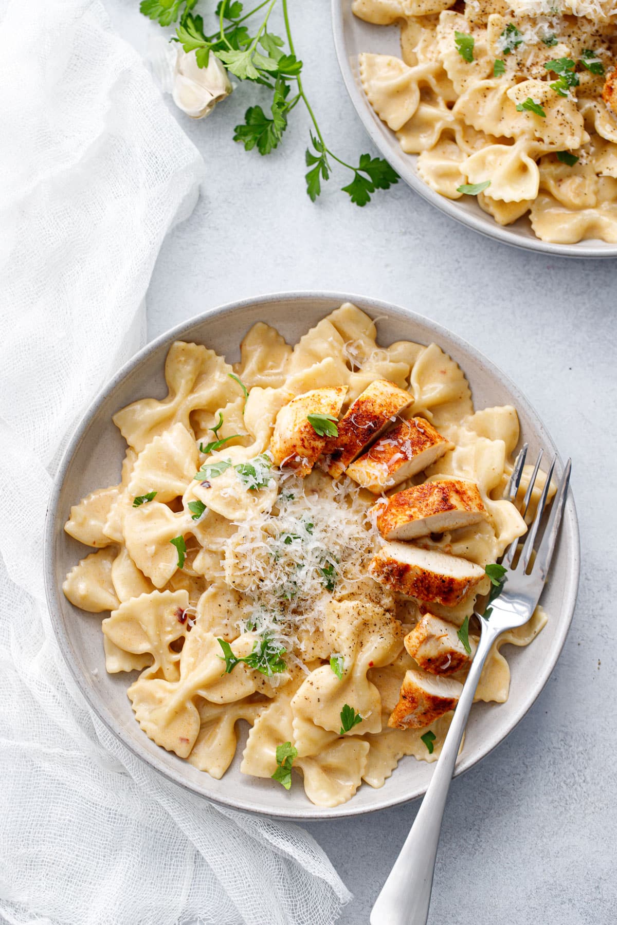 Overhead, bowl of Creamy Garlic Chicken Pasta with a cut chicken tender that is nicely browned, and a pile of grated parmesan.