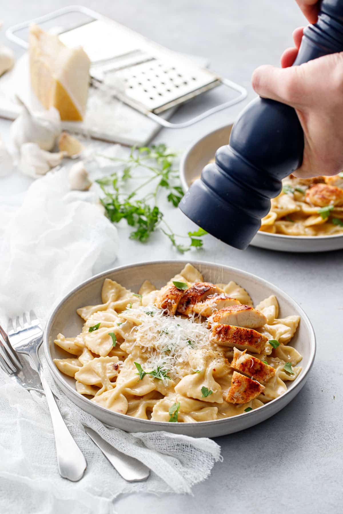 Blue pepper grinder grinding fresh pepper on top of a bowl of Creamy Garlic Chicken Pasta.