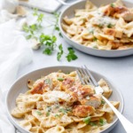 Two shallow bowls with Creamy Garlic Chicken Pasta, napkin and forks and a piece of parmesan cheese in the background.