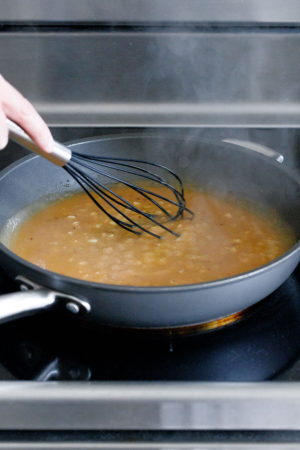Whisking the chicken broth into the pan sauce until thickened, visible chunks of minced garlic.