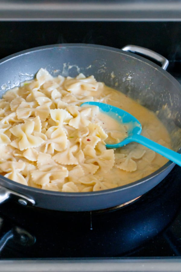 Saucepan with pasta before serving, farfalle noodles coated with a creamy garlicky sauce and a silicone serving spoon.