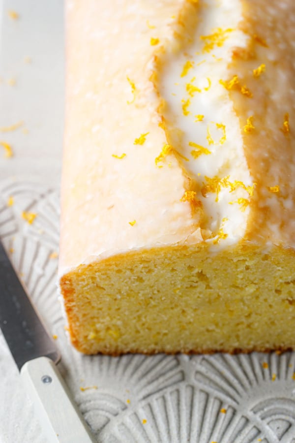 Closeup, cut Meyer Lemon Olive Oil Loaf Cake from a high angle, showing the top of the cake with a thin white sugar glaze and a sprinkle of zest on top.