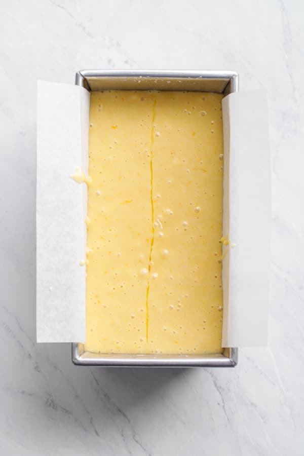 Overhead, loaf pan filled with batter before baking, showing the 'seam' of olive oil down the center.