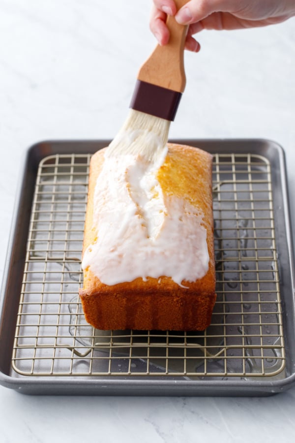 Using a pastry brush to coat the entire cake with a white powdered-sugar based glaze.