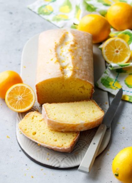 Meyer Lemon Olive Oil Loaf Cake with two slices cut to show the interior texture, whole/half lemons, napkin and a knife around it.