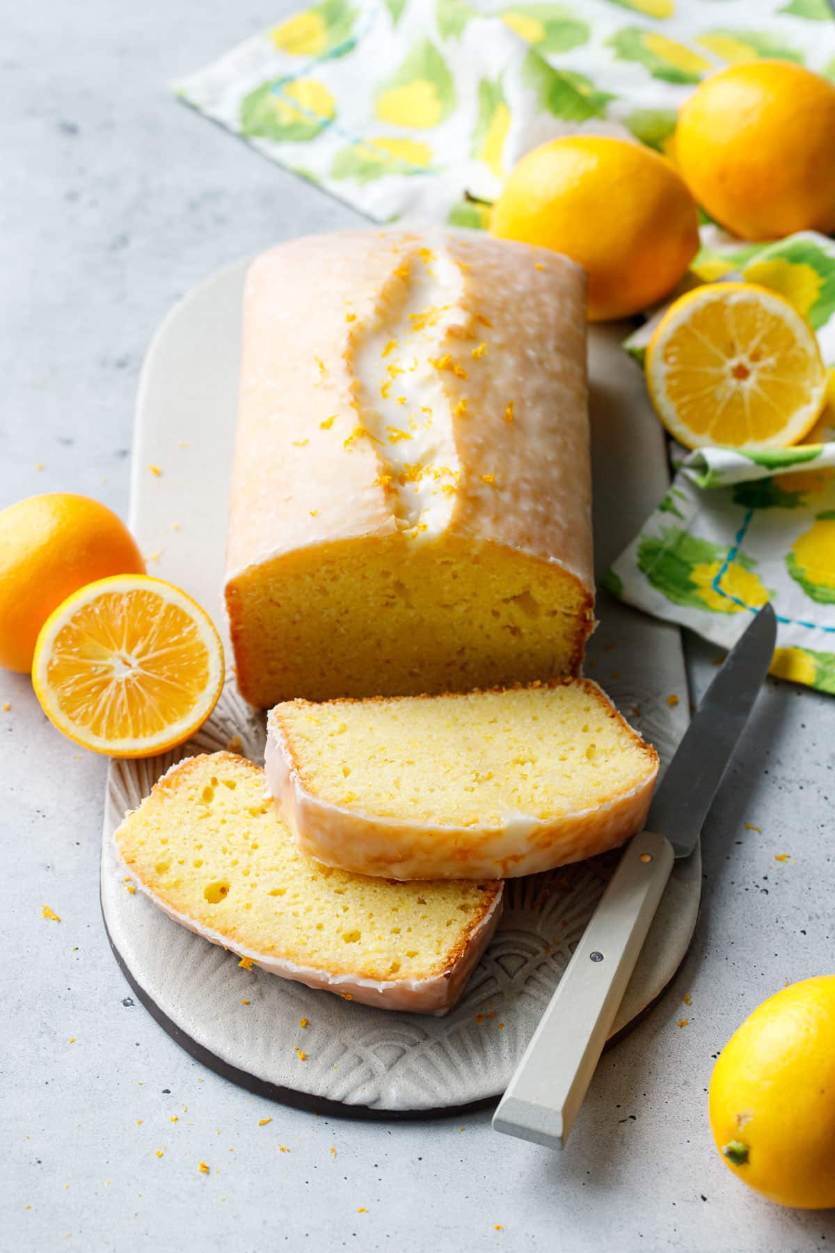 Meyer Lemon Olive Oil Loaf Cake with two slices cut to show the interior texture, whole/half lemons, napkin and a knife around it.