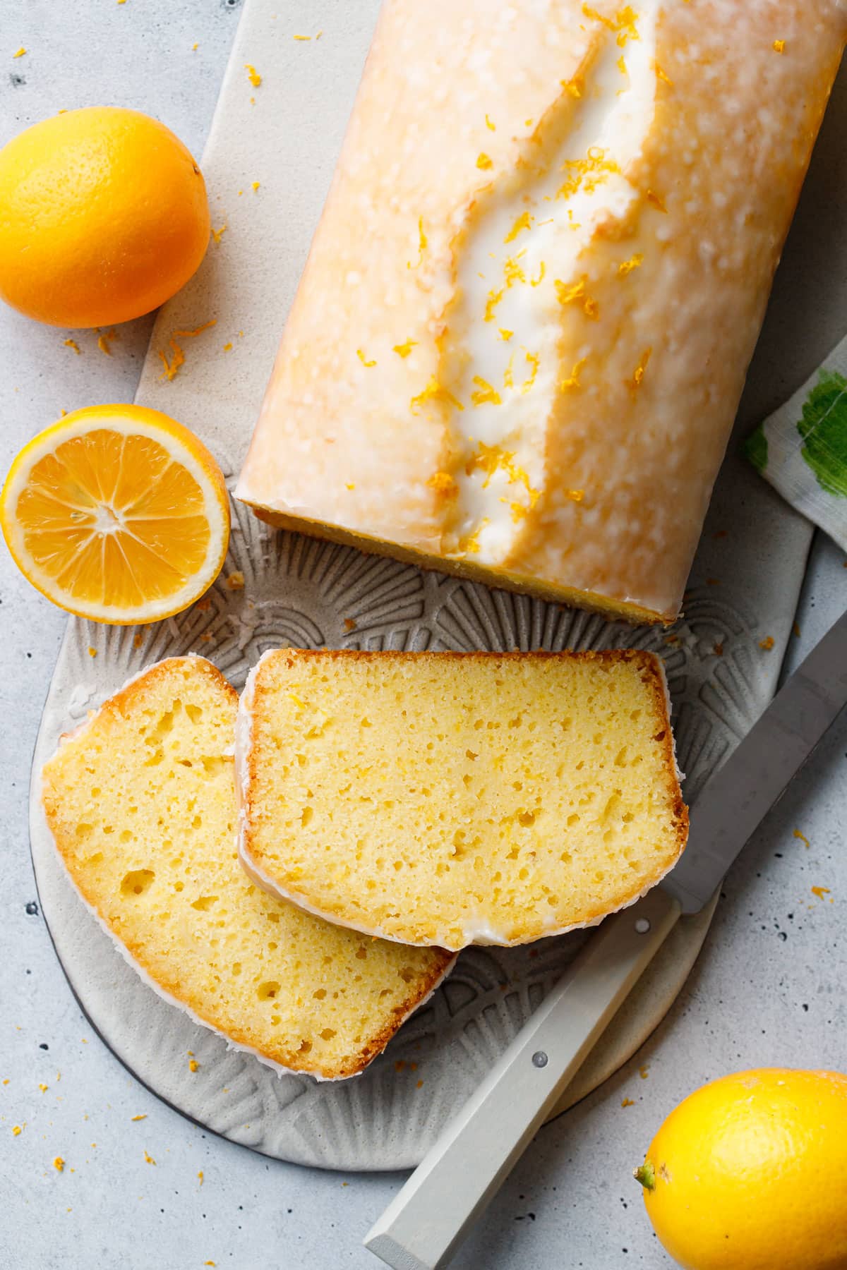 Overhead, two slices of Meyer Lemon Olive Oil Loaf Cake cut and laying down to show the interior texture, with Meyer lemons and a knife.