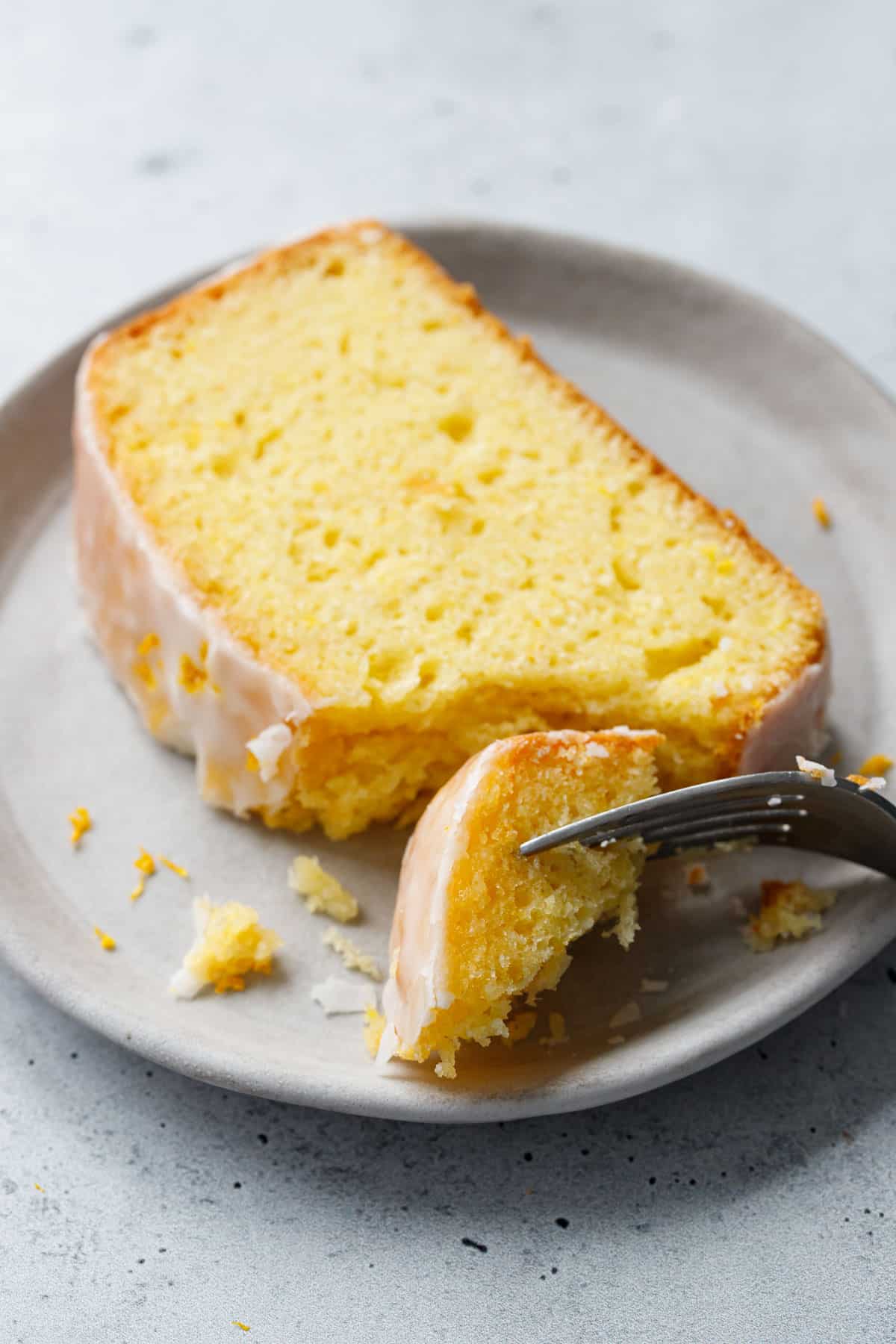 Closeup, slice of Meyer Lemon Olive Oil Loaf Cake with a forkful taken out of it to show the texture, crumb, and crackly sugar glaze on the outside.