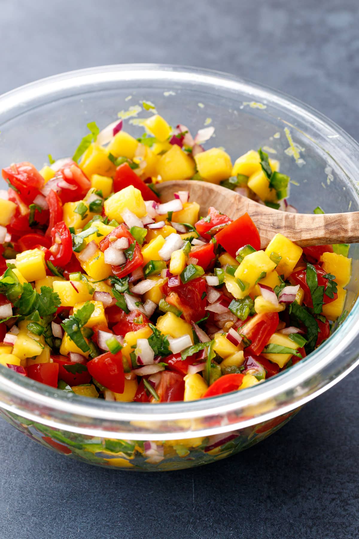 Glass bowl with freshly made mango salsa, with visible chunks of cherry tomato, red onion and cilantro.