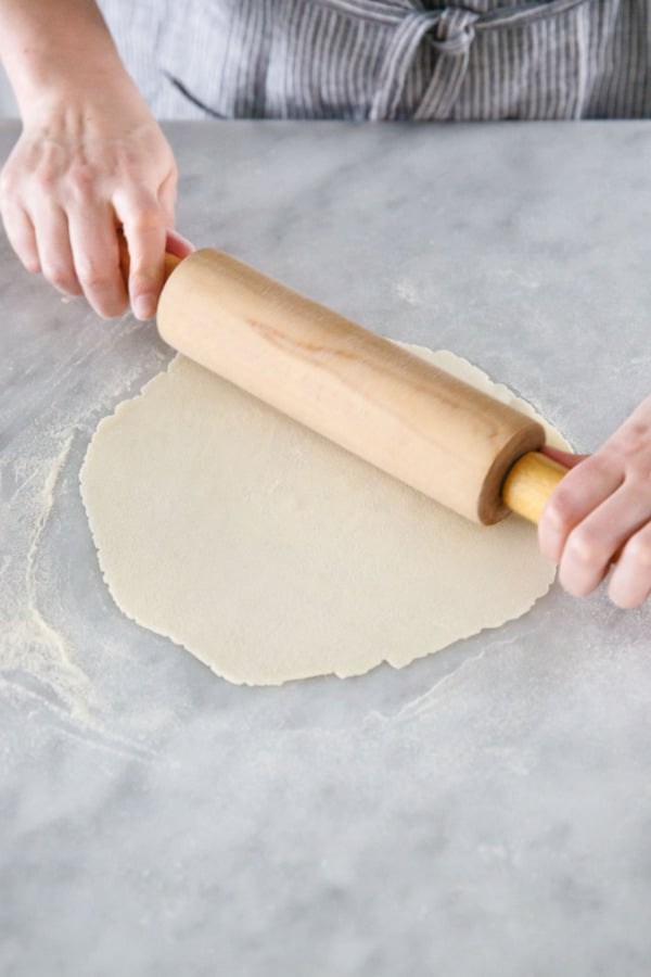 Rolling the semolina cracker dough as thin as possible with a rolling pin.