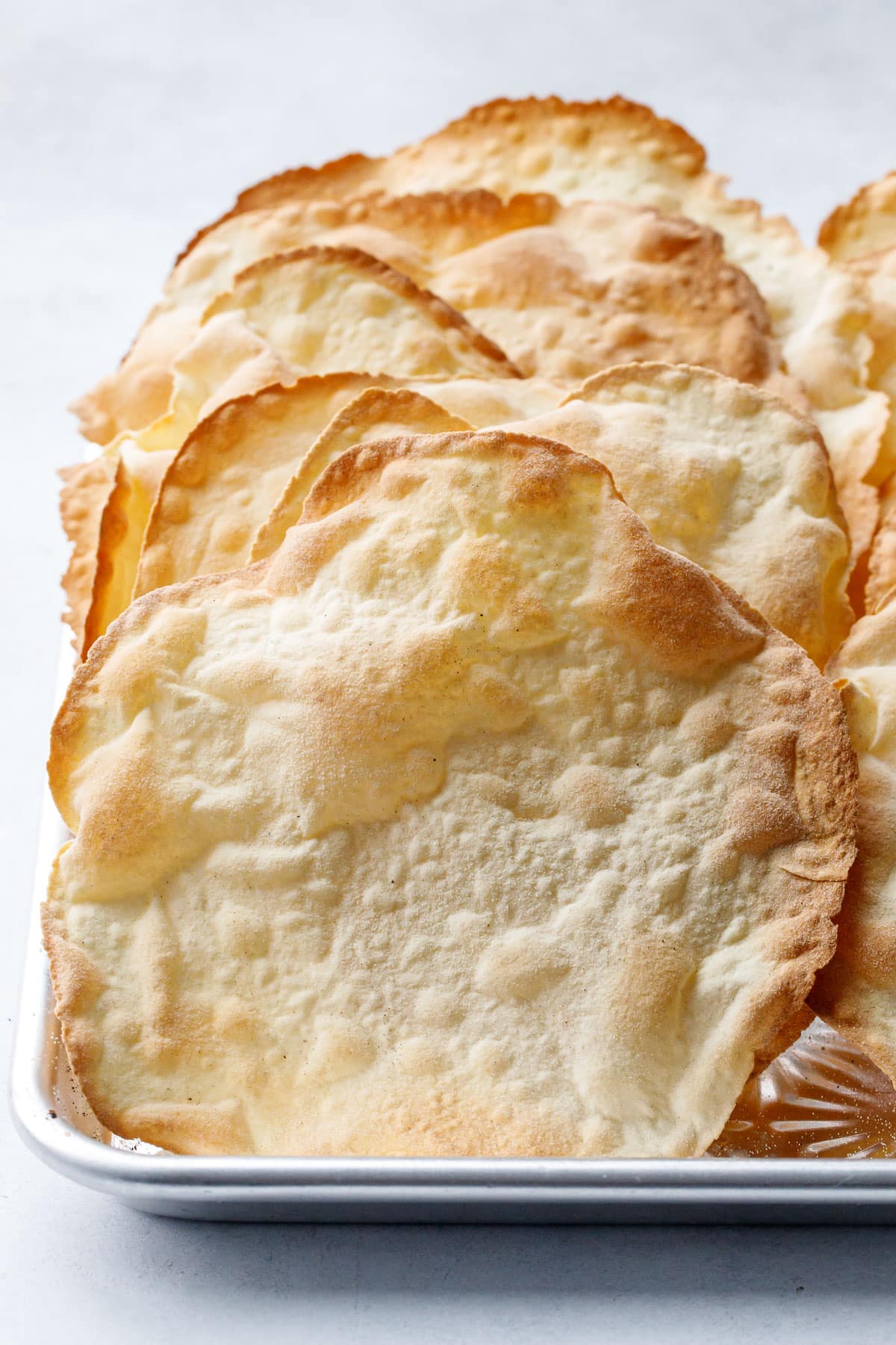 Row of baked sourdough semolina parchment crackers, close up shot showing the bubbly surface, super thin texture and golden brown edges.