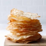 Side view stack showing just how thin and crispy these semolina sourdough crackers are, stack sitting on a distressed wooden bread board.
