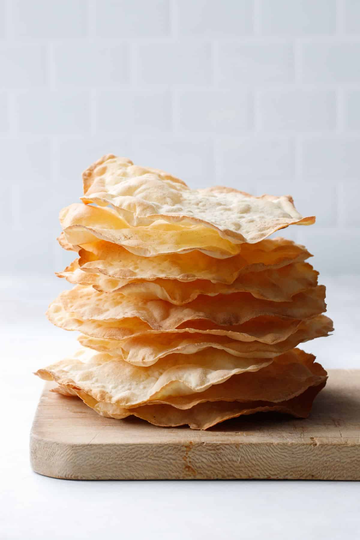 Side view stack showing just how thin and crispy these semolina sourdough crackers are, stack sitting on a distressed wooden bread board.