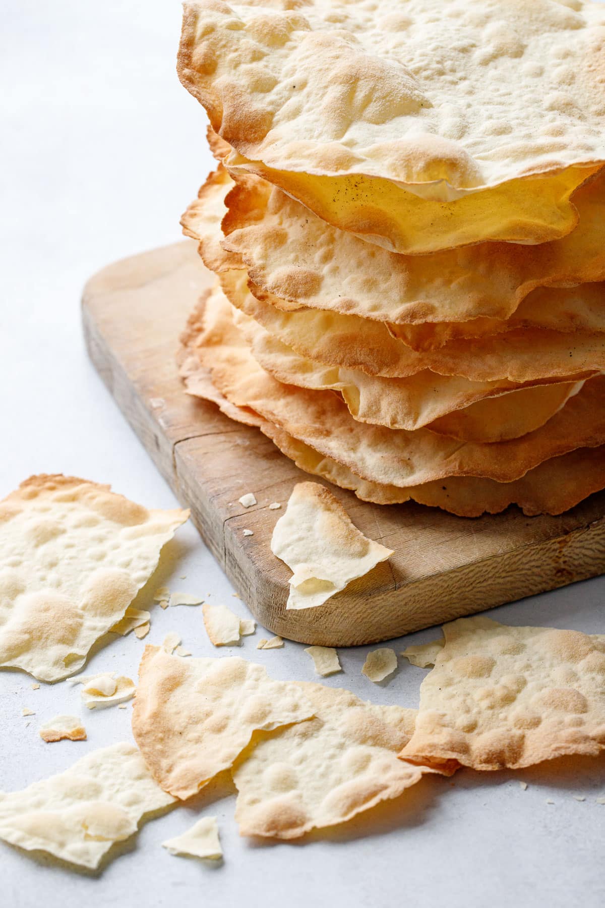 Stack of Sourdough Semolina Parchment Crackers on a board, with broken pieces of cracker scattered about showing just how thin and crispy the texture is.