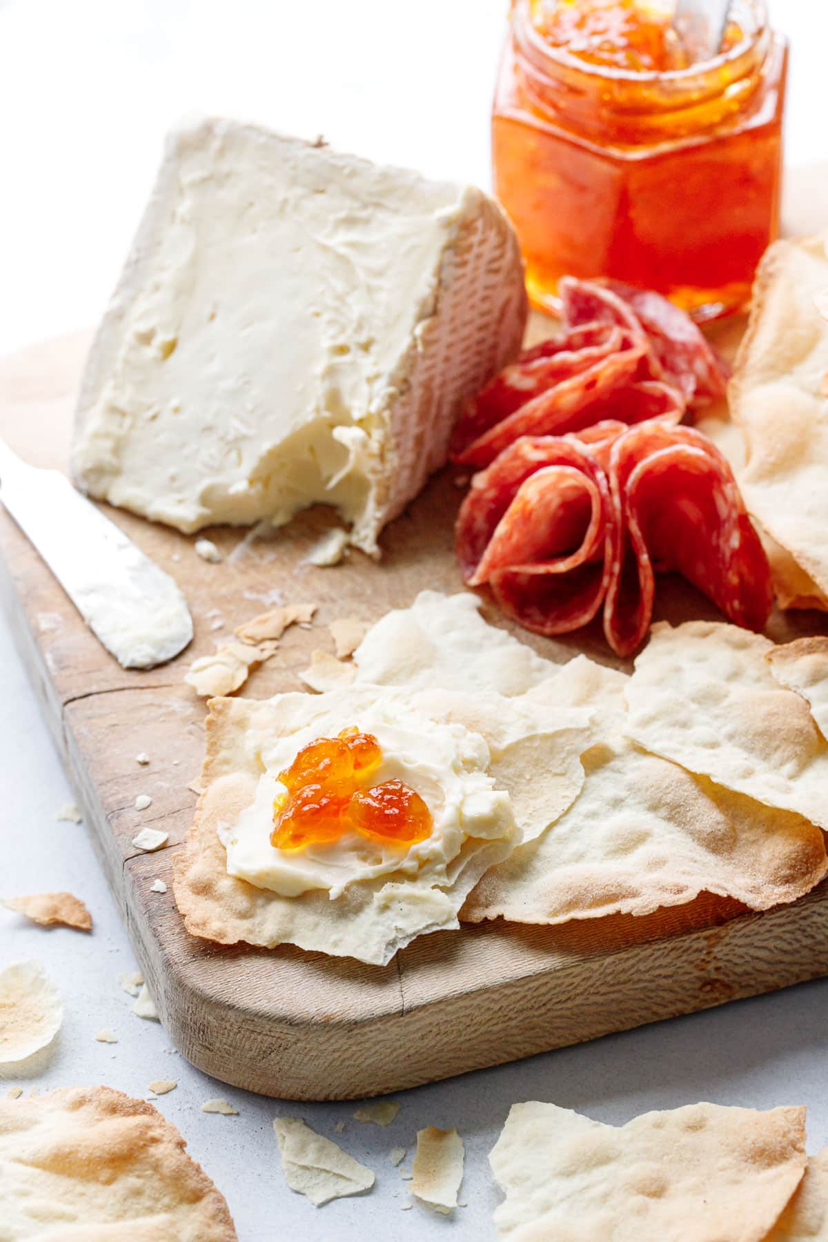 Sourdough Semolina Parchment Crackers on a wooden board, one broken piece of cracker spread with soft chese and a dollop of pepper jelly.