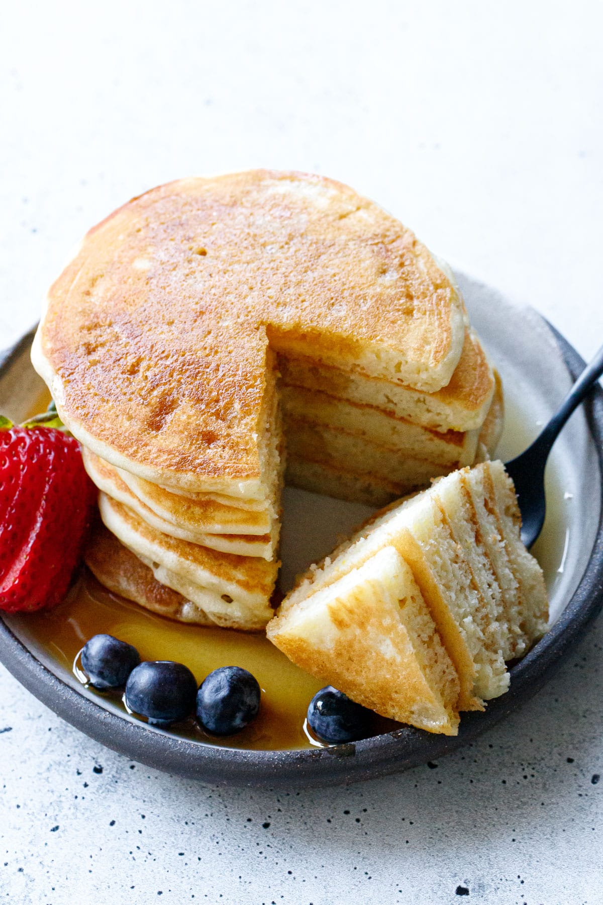 Stack of Olive Oil Pancakes with a wedge cut out on a fork to show the fluffy interior texture.
