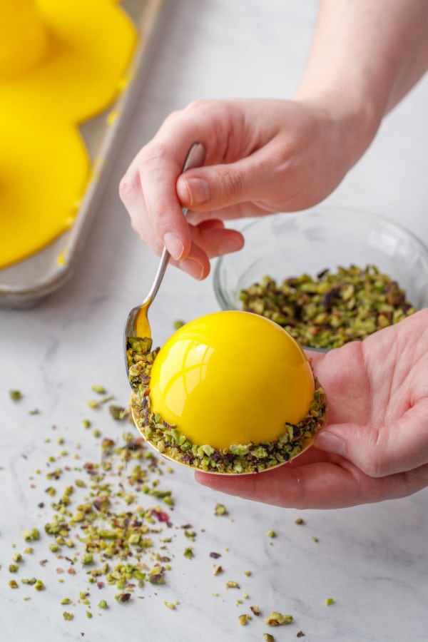 Coat the lower rim of the glazed cakes with chopped pistachios for a decorative finish.